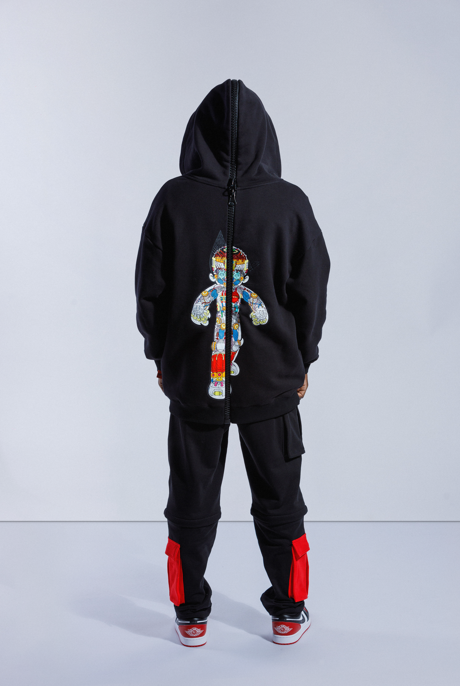 Back of model wearing Black Astro Boy zip hoodie with hood up, with large black zip down the middle and Astro Boy graphic showing his internal mechanism