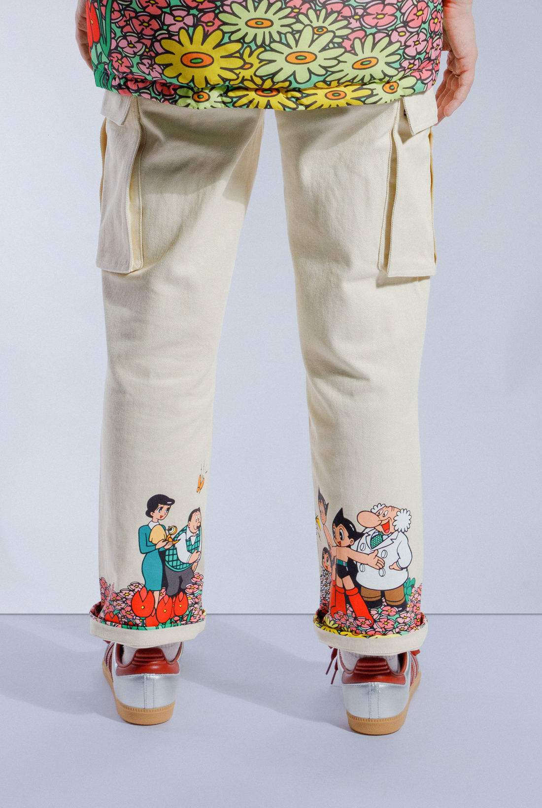 Cream Astro Boy Jeans with screen printed graphic wrap around the bottom of both pant legs. Graphic shows Astro Boy and his family in a field of flowers