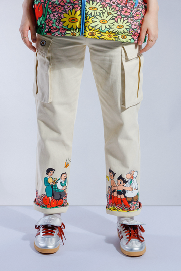 Cream Astro Boy Jeans with screen printed graphic wrap around the bottom of both pant legs. Graphic shows Astro Boy and his family in a field of flowers