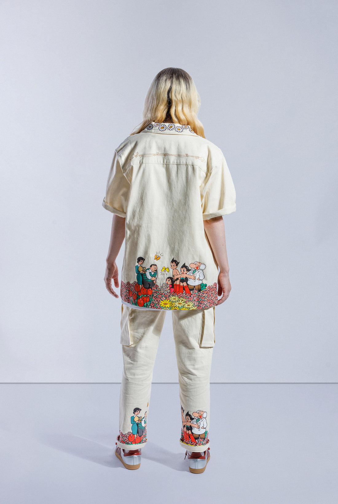 Model wearing cream Astro Boy button up shirt. Features a screen printed graphic that wraps around the bottom shirt. The graphic shows Astro Boy and his family in a field of flowers