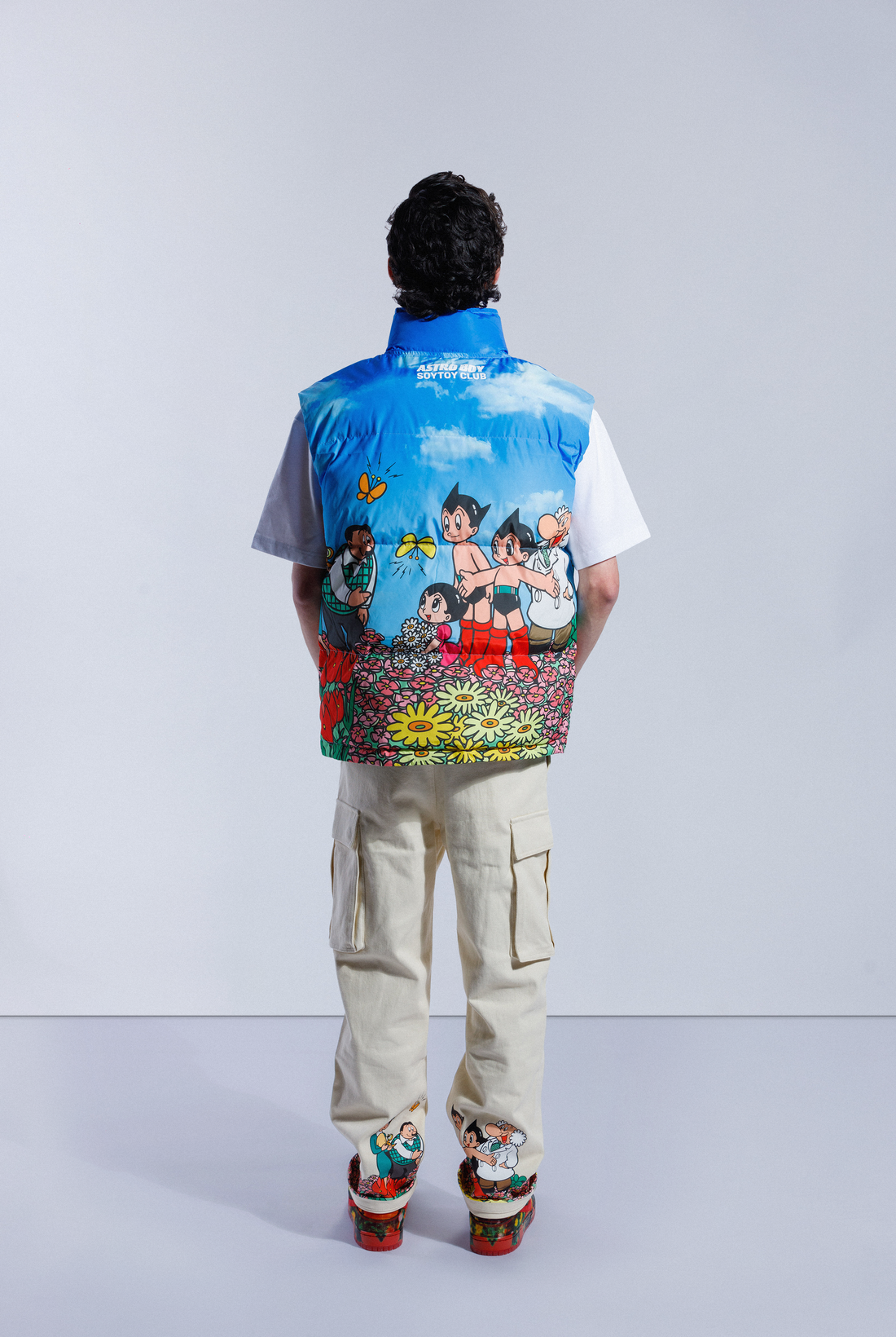 Model wearing the blue Astro Boy Family Portrait Puffer Vest. Features a graphic showing Astro Boy and his family in a field of flowers