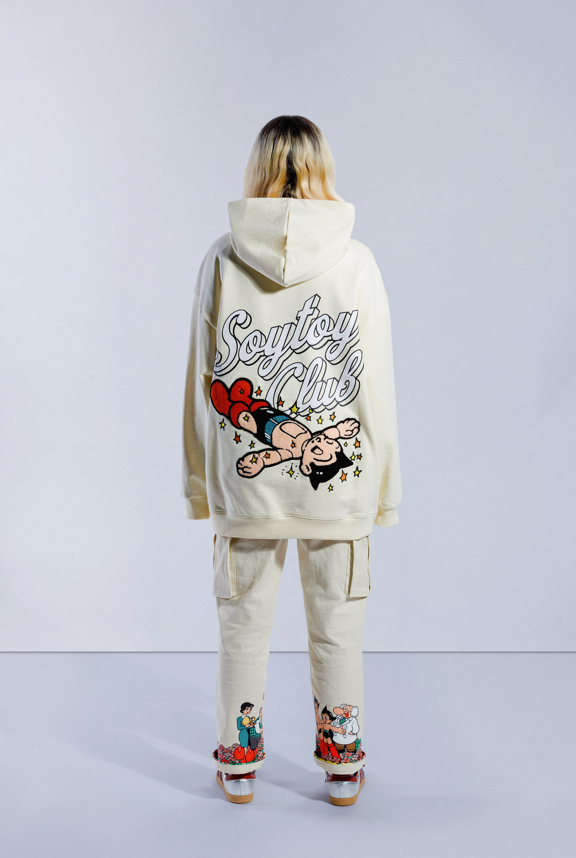 Back of model wearing Sleepy Boi hoodie. Shows large Soytoy Club text with chenille embroidered Astro Boy sleeping in a field of stars