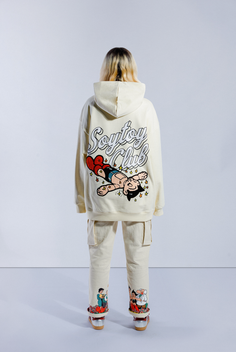 Back of model wearing Sleepy Boi hoodie. Shows large Soytoy Club text with chenille embroidered Astro Boy sleeping in a field of stars