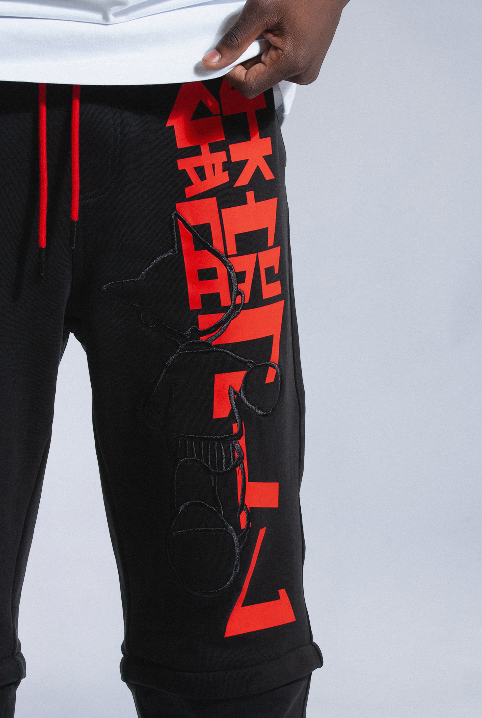 Close up of Astro Boy trackpants. Shows red screenprint logo, black embroidered astro boy logo and red drawstrings