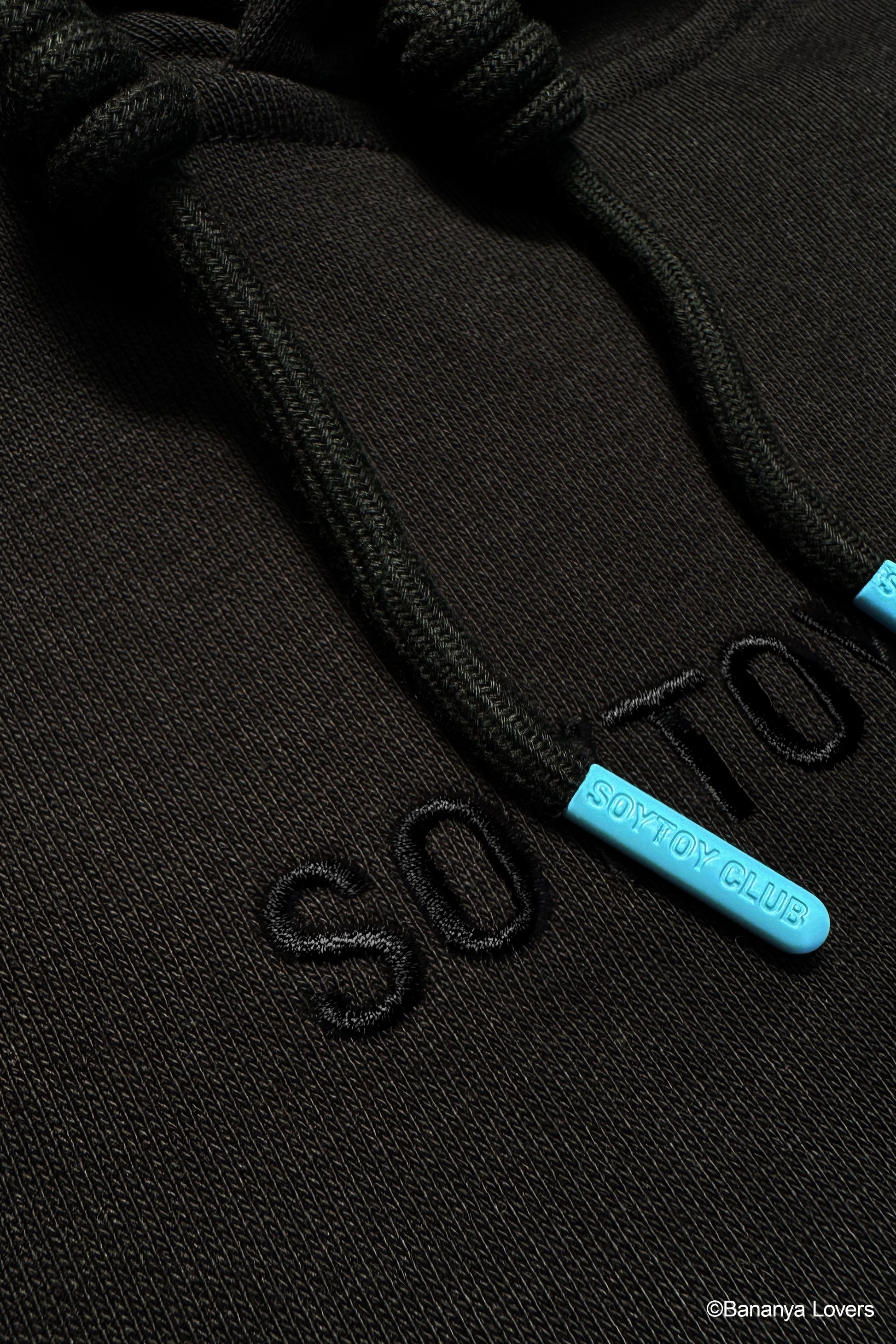 Close-up of a black hoodie with blue 'Soytoy club' aglets