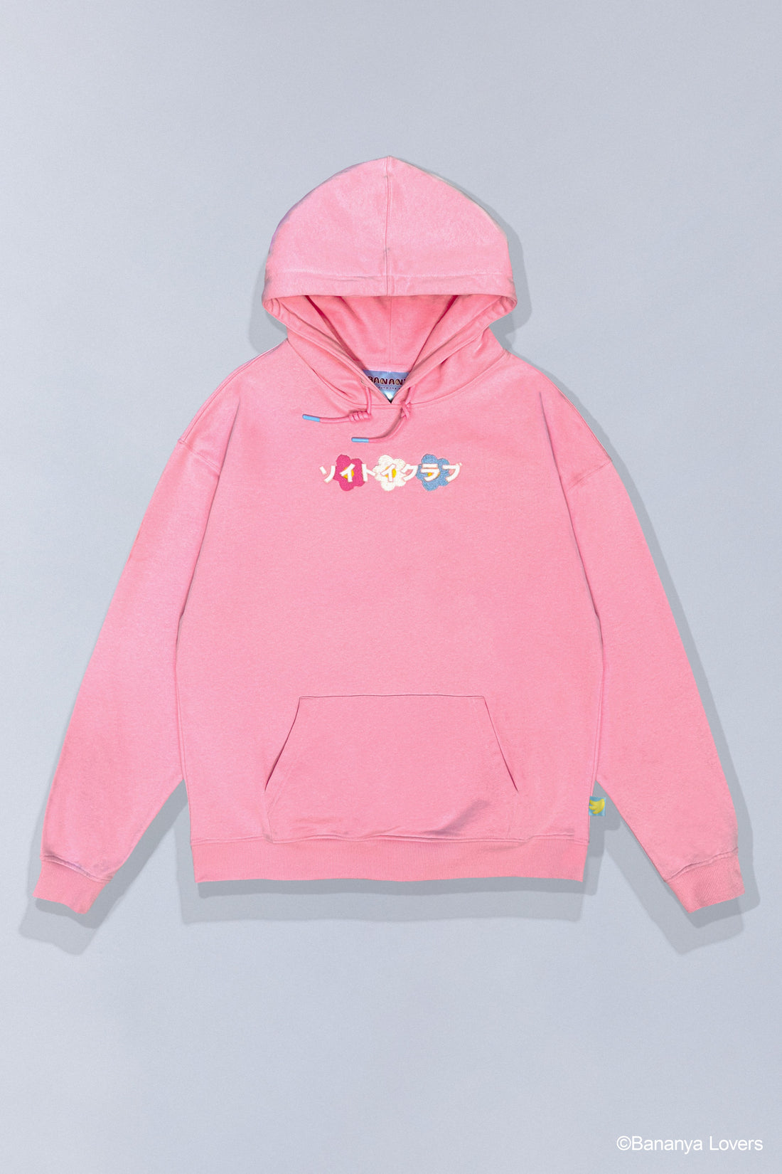 Pink SOYTOY CLUB hoodie featuring embroidered Bananya the white cartoon cat sitting inside a yellow banana on top of  coloured flowers. Hoodie is on a light gray background