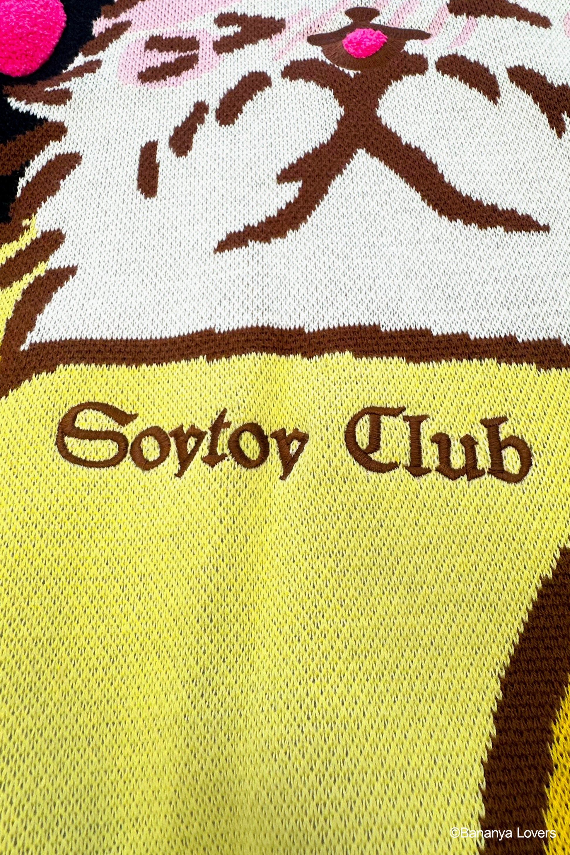 Close up of black knit Bananya sweater. shows embroidered 'soytoy club' text on front of knit