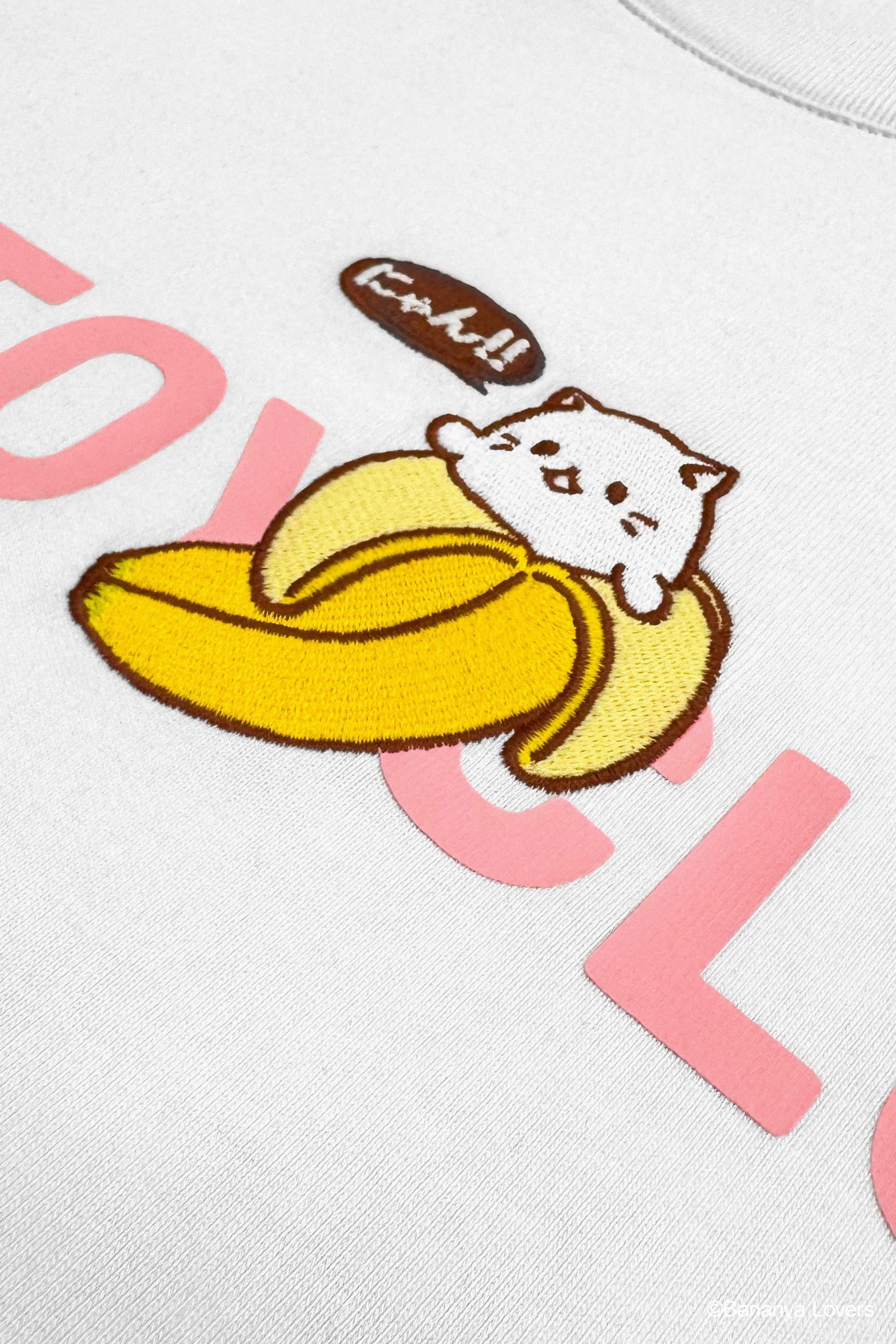 Detail of white Bananya Logo t-shirt. Shows pink 'SOYTOY CLUB' text with embroidered Bananya cat on top.